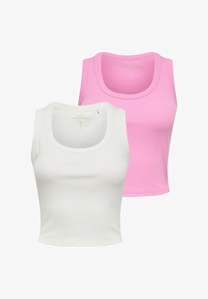 Kvinde smilende iført hvid ærmeløs top, mørke vidde jeans med sort nittebælte, der holder en sort håndtaske, mens hun går.