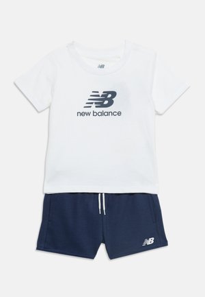Biała koszulka New Balance z krótkim rękawem oraz granatowe szorty z troczkiem i logo na lewej nogawce.