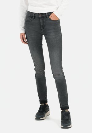 Schlanke, dunkelgraue Jeans mit einem verblassten Design, fünf Taschen und umgeschlagenen Säumen, kombiniert mit dunklen Turnschuhen und einem weißen Langarmshirt.