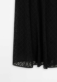 Jupe noire avec un motif en dentelle diamant texturé et un ourlet légèrement transparent sur fond blanc.