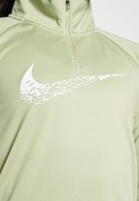 Ljust grön zip-up träningsskjorta med en vit Nike swoosh-logotyp med en texturerad design, tillverkad av ett slätt, sträckbart tyg.
