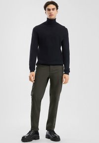 Maglione a collo alto blu navy, pantaloni attillati verde scuro e stivali neri con lacci. Design semplice, texture liscia e palette di colori coerente.