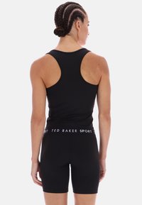 Fekete sportos tank top, racerback dizájnnal és fekete rövidnadrággal. Jellemzője a márkázott elasztikus derékpánt. Simább, rugalmas szövettextúra.