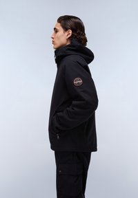 Giacca softshell nera con cappuccio, tasche laterali con zip, polsini elasticizzati e toppa con logo sulla manica sinistra. Tessuto resistente e design elegante.