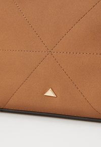 Brunt tekstureret materiale med sydde geometriske mønstre og en gylden trekantet accent i bunden. Glat finish, elegant design.