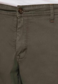 Pantaloni din bumbac verde măsliniu, cu închidere frontală cu nasture, buzunare laterale și accente cusute, cu o textură fină și o croială ajustată.
