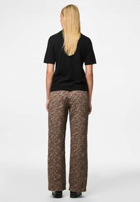 Crna košulja kratkih rukava u kombinaciji s smešnim hlačama širokih nogavica od naboranog materijala, s diskretnim uzorkom i ravnim obućom.