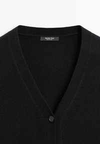 Svart ullkofta med V-ringning, med en enda knappstängning och mjuk textur. Etiketten lyder "Massimo Dutti, Tillverkad i Kina."