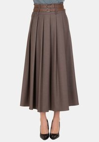 Gonna midi plissettata marrone con cintura a doppia fibbia, indossata con décolleté nere con punta appuntita su sfondo neutro.