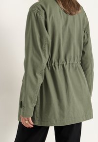 Chaqueta verde oliva hecha de un tejido resistente, con cintura ceñida, mangas largas y puños abotonados. Diseño minimalista sin patrones visibles.