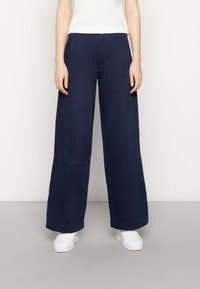 Marina vida byxor i bred benstil, tillverkade av en bomullsblandning, med hög midja, sidofickor och en mjuk textur. Kombineras med vita sneakers.