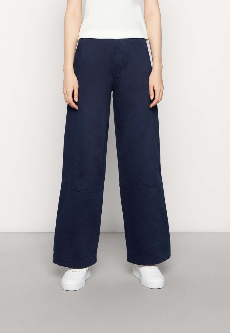 Marina vida byxor i bred benstil, tillverkade av en bomullsblandning, med hög midja, sidofickor och en mjuk textur. Kombineras med vita sneakers.