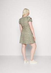Vestido floral verde com mangas curtas em balão, apresentando um corpete justo e uma saia ampla. Combinado com sapatilhas de cor clara.