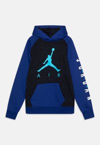 Blå hoodie med ett svart prickigt mönster. Har en turkos Jumpman-logotyp, texten "AIR" och "JORDAN" på ärmen. Frontficka ingår.