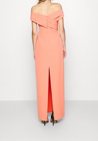 Coral off-the-shoulder gown with a fitted bodice, a split at the back, and a smooth texture. Features layered draping at the shoulders.