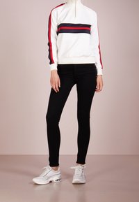 Vit zip-hals tröja med röda och marinstreifen, svarta skinny jeans och vita sneakers med synlig luftdämpning.