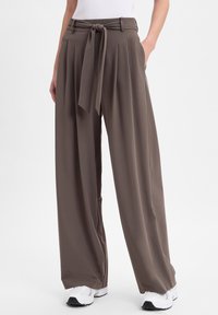 Sandfarbene weite Hosen mit einem gebundenen Bund, Falten und Taschen. Hergestellt aus einem glatten, leichten Stoff.