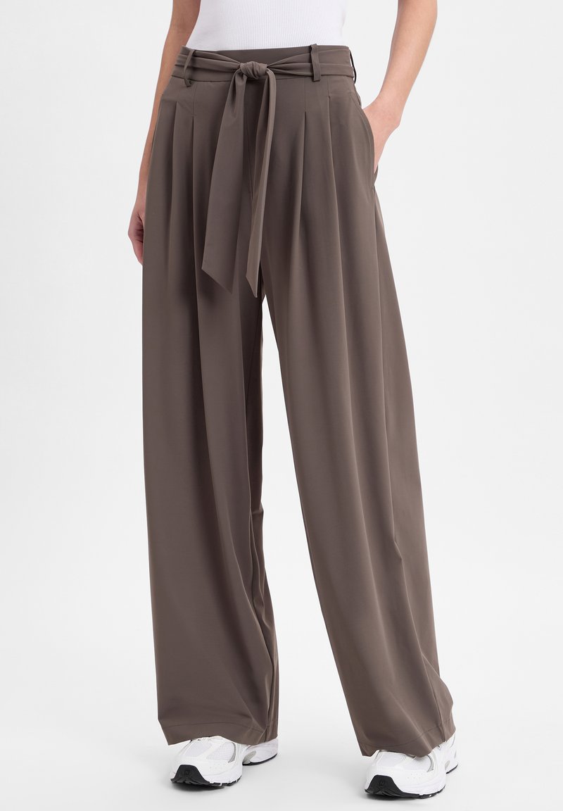 Sandfarbene weite Hosen mit einem gebundenen Bund, Falten und Taschen. Hergestellt aus einem glatten, leichten Stoff.