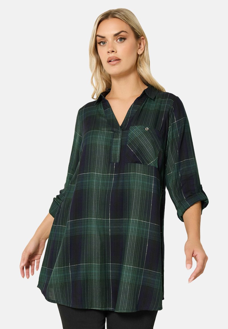 Zielona koszula w kratę, wykonana z lekkiego materiału, z dekoltem w serek, kieszenią na piersi i podwiniętymi rękawami. Wzór składa się z ciemnozielonych i jasnzielonych odcieni.
