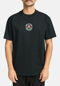 Camiseta de algodón negra con cuello redondo, que presenta un gráfico central de una rosa y un logotipo en colores suaves. Mangas cortas, corte relajado.