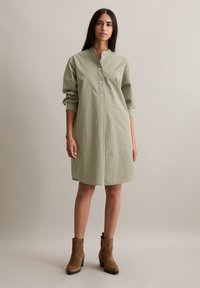 Groene gingham jurk, met kraag, knoopsluiting aan de hals, lange mouwen, net boven de knie, gemaakt van lichtgewicht stof. Bruine enkellaarzen maken de outfit compleet.