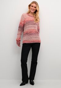 Maglione lavorato a maglia in tonalità di rosa e viola con un motivo testurizzato, colletto rotondo e maniche lunghe, abbinato a pantaloni neri a palazzo e stivali con tacco.