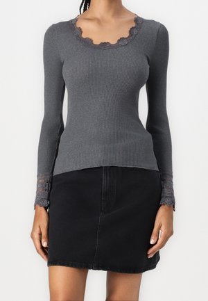 Mujer con un top gris ajustado de manga larga acanalada, con encaje en el escote y los puños, combinado con una minifalda de mezclilla negra.