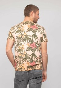T-shirt à manches courtes de couleur rose avec un motif floral tropical, présentant des feuilles vertes et des fleurs rosées, fabriqué en tissu doux.