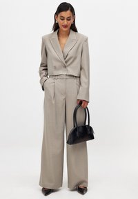 Lühi beez bleiser kahekordsete nööpidega, laiad püksid ja väike must käekott. Sile kangas, kohandatud lõige ja minimaalne detail.