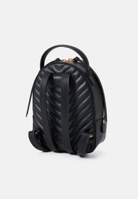 Svart skinn mini ryggsekk med et kviltet herringbone-mønster, gull hardware, doble stropper og glidelås på toppen.