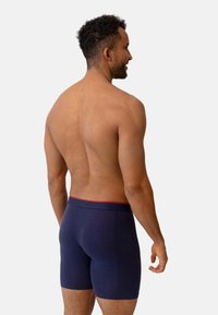 Marinblå boxershorts med en mjuk textur, med en åtsittande design och en kontrasterande röd midjeband. Utsikt bakifrån.