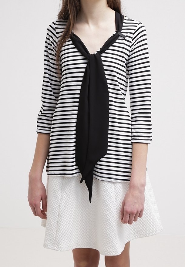 Randig svart och vit topp med en halsknut, i kombination med en texturerad vit kjol. Har trekvartsärmar och en avslappnad passform.