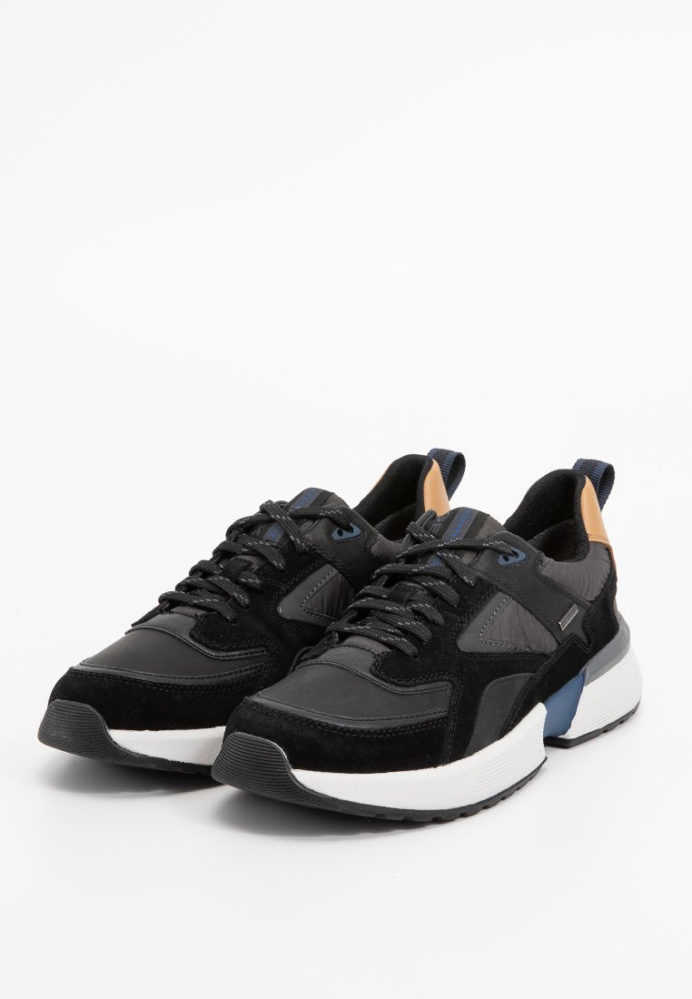 Schwarze Sportschuhe aus einer Mischung aus Wildleder und synthetischen Materialien. Sie verfügen über eine weiße Zwischensohle, blaue und beige Akzente sowie strukturierte Details.