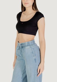 Top corto nero a coste con scollatura a girocollo, maniche corte, caratterizzato da un piccolo dettaglio logo rosso, bianco e blu sul petto.