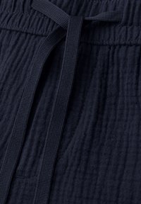Tissu texturé bleu marine avec un cordon plat noué sur une taille élastique, montrant des coutures détaillées et la texture du matériau.