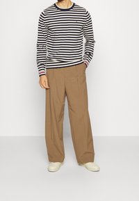 Chemise à manches longues rayée bleu marine et crème avec un col rond, associée à un pantalon large marron et des baskets de couleur claire.