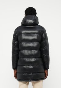 Black puffer jacket with a glossy finish, horizontal quilted design, an attached hood, and a knee-length cut.