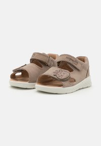 Beige nahkakengät avonaisella varpaalla, säädettävällä hihnalla ja koristeellisella eläinkuvioinnilla. Valkoinen teksturoitu pohja tarjoaa pitoa ja mukavuutta.