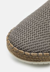 Grau gestalteter Mesh-Schuh mit strukturierten Oberflächen, runder Zehenpartie und geflochtenem, strohähnlichem Akzent entlang der Sohle.