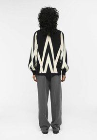 Maglione a righe bianche e nere con un design geometrico, abbinato a pantaloni grigi a gamba larga. Dettagli in tessuto morbido e textured.