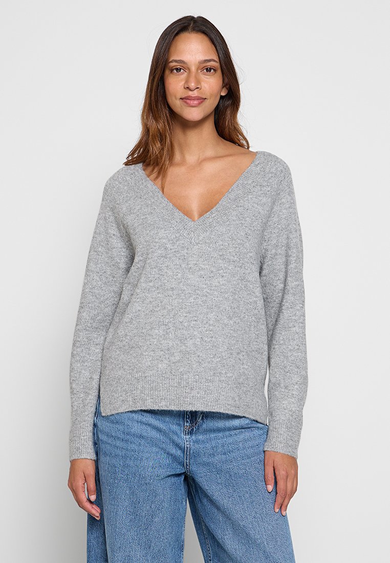 Grijze v-hals trui van zacht breiwerk; met lange mouwen en een relaxte pasvorm. Draag met lichtblauwe jeans.