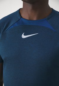 Marinblå sportt-shirt med strukturerad tyg, med en enfärgad blå axelpane och en vit Nike-logga på bröstet.