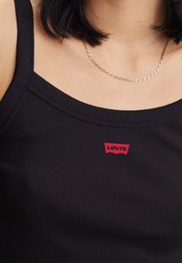 Černý žebrovaný top bez rukávů s červeným logem Levi's na výstřihu. Hladká textura s širokými ramínky a přiléhavým střihem.