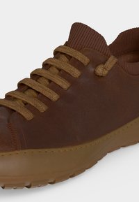 Sneaker en cuir marron avec des lacets couleur havane, un col côtelé marron et une semelle en caoutchouc texturée, vue de près de côté.