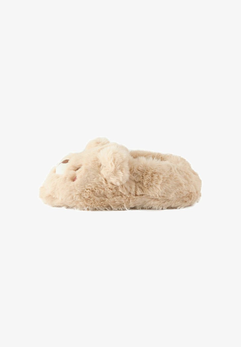 Chausson doux beige en peluche en forme d'ours en peluche avec des oreilles et un visage sur le devant, vu de côté sur fond blanc.