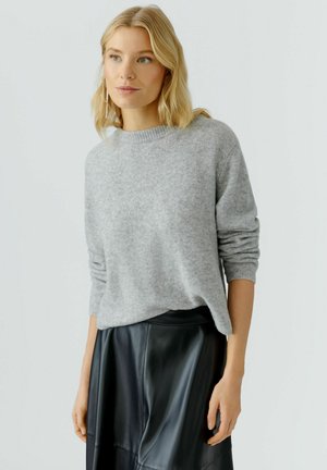Pull en maille gris clair avec un col rond côtelé et des manches longues, associé à une jupe en cuir noire. Texture douce, coupe décontractée.