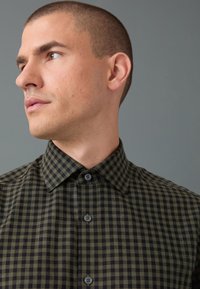 Camicia a quadri verde e nera con bottoni e colletto classico, caratterizzata da tessuto strutturato e bottoni grigi, dallo stile aderente.