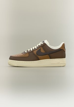 Baskets Nike Air Force 1 en cuir marron et beige avec lacets blancs et semelle écrue, vues de côté sur un fond uni.