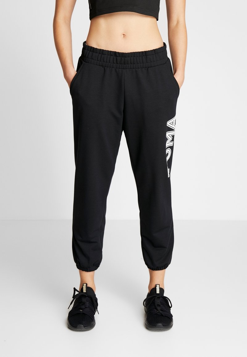 Zwarte sweatpants met een elastische tailleband, taps toelopende boorden en het "PUMA"-logo in het wit op het linkerbeen. Het materiaal lijkt zacht en rekbaar.