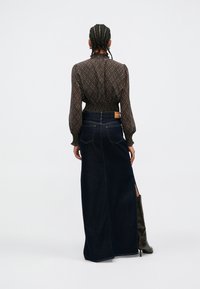 Pruun mustriline pluus pihavarrukatega, kombineeritud tumeda teksase maxi seelikuga, millel on kõrge lõhik ja taga vöökoha silt.